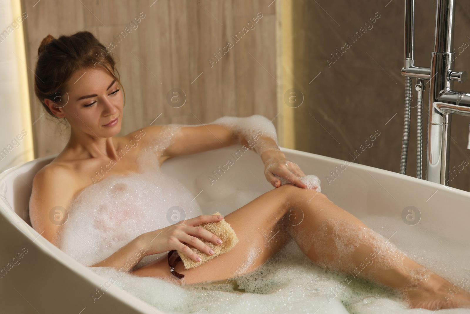 Photo of Beautiful woman with loofah taking bath indoors