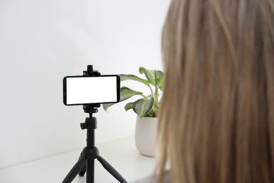 Woman with smartphone fixed to tripod indoors. Mockup for design