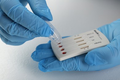 Photo of Doctor dropping buffer solution onto disposable multi-infection express test cassette at white table, closeup