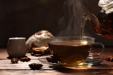 Pouring aromatic anise tea into glass cup on wooden table