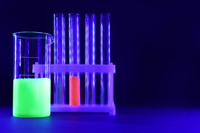 Laboratory glassware with luminous liquids on dark blue background, space for text