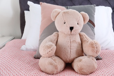 Cute teddy bear sitting on bed indoors