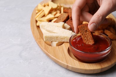 Woman dipping crispy rusk in sauce at light marble table, closeup. Space for text