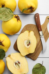 Tasty ripe quince fruits and knife on white wooden table, flat lay