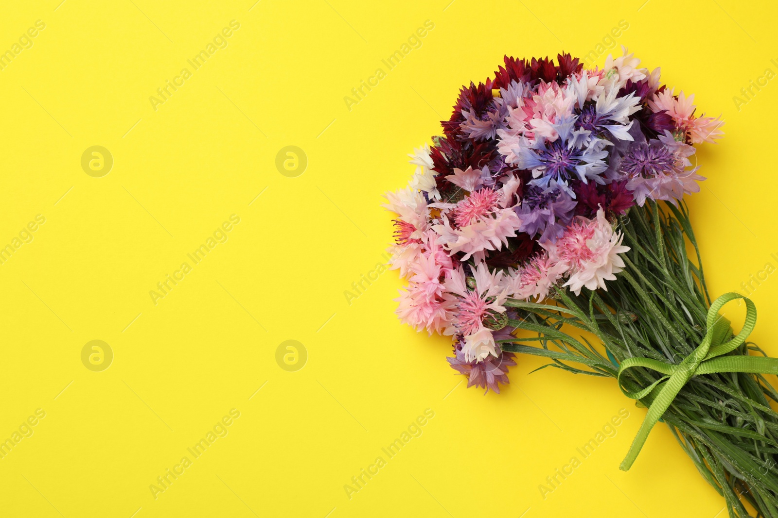 Photo of Bouquet of beautiful colorful cornflowers on yellow background, top view. Space for text