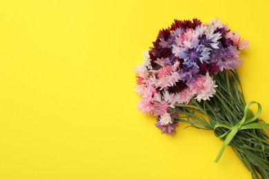 Photo of Bouquet of beautiful colorful cornflowers on yellow background, top view. Space for text