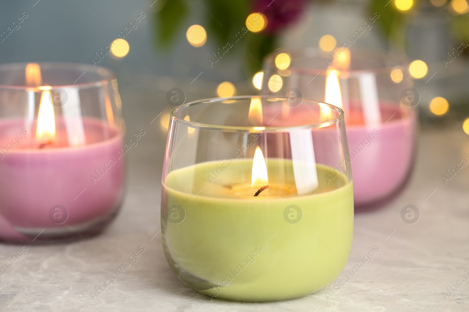 Photo of Burning candles in glass holders on grey table against blurred lights