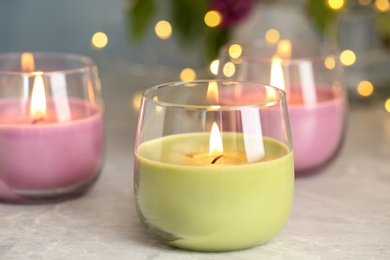 Photo of Burning candles in glass holders on grey table against blurred lights