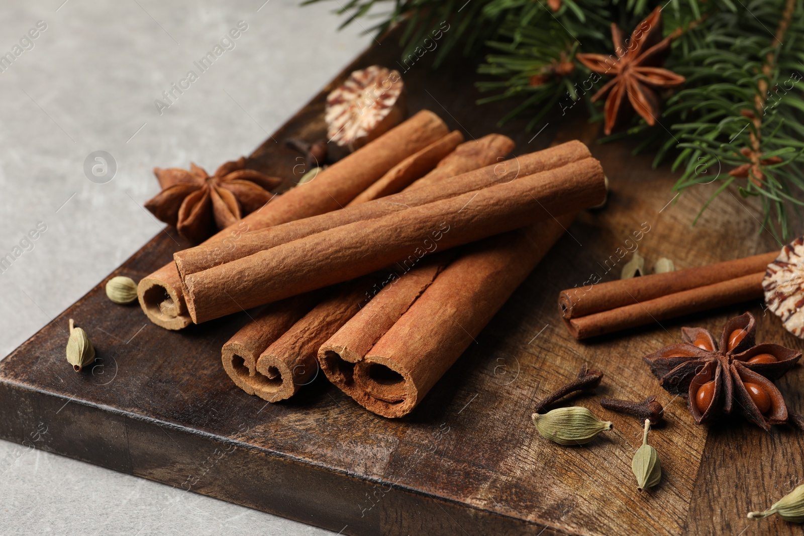 Photo of Board with different aromatic spices and fir branches on light table, closeup