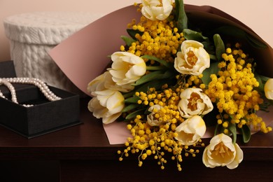 Bouquet with beautiful spring flowers and necklace on wooden chest of drawers, closeup