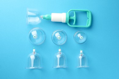 Plastic cups and hand pump on light blue background, flat lay. Cupping therapy