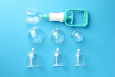 Photo of Plastic cups and hand pump on light blue background, flat lay. Cupping therapy