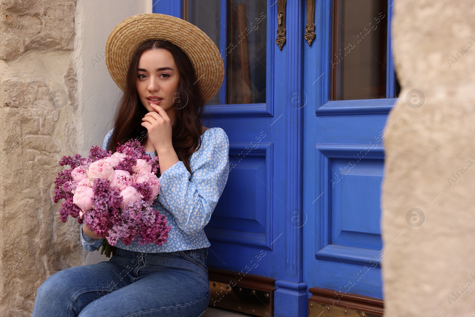 Photo of Beautiful woman with bouquet of spring flowers near building outdoors, space for text