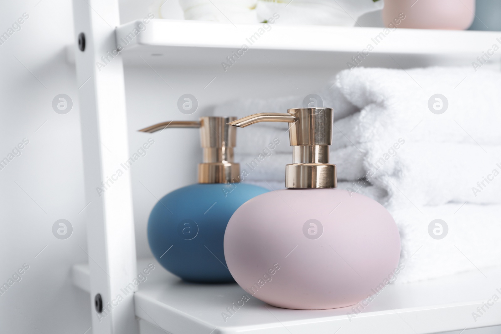 Photo of Stylish soap dispensers and towels on shelf near light wall