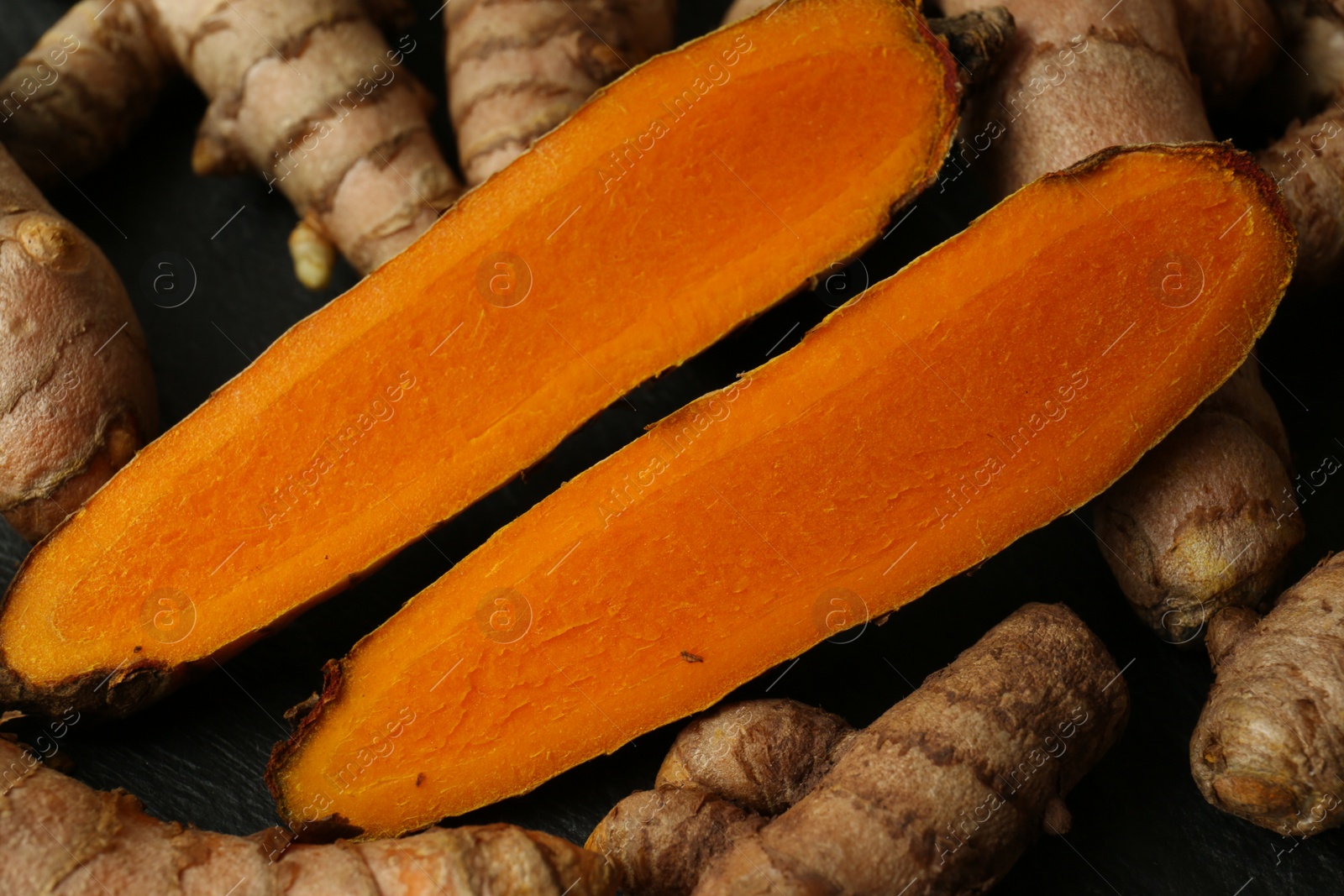 Photo of Whole and cut turmeric roots on table, closeup