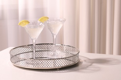 Tray with martini glasses of fresh cocktail and lemon slices on white table indoors. Space for text