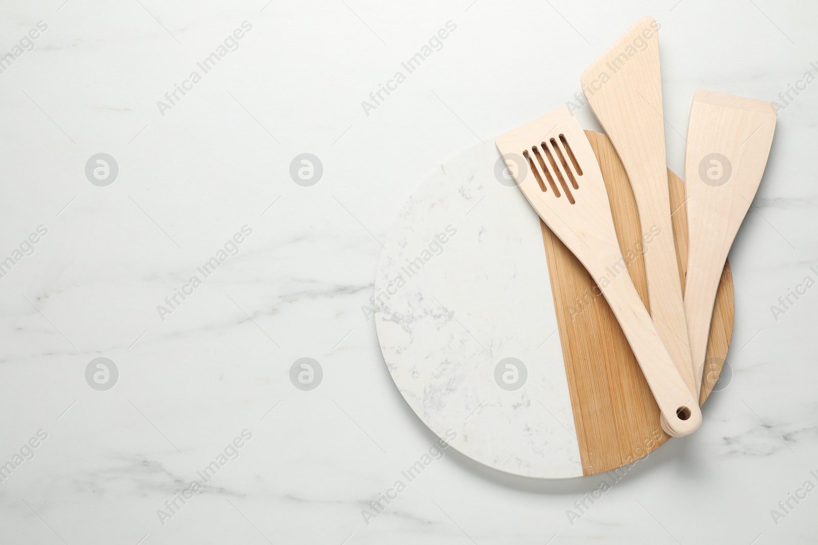 Photo of Board with different wooden spatulas on light marble table, top view. Space for text