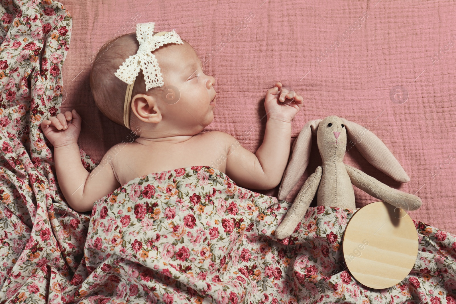 Photo of Cute newborn baby girl with toy on pink bedsheet, top view