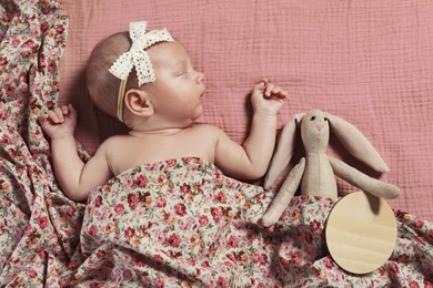 Photo of Cute newborn baby girl with toy on pink bedsheet, top view