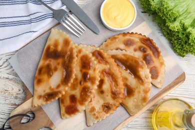 Photo of Delicious fried chebureki with sauce on white wooden table, flat lay