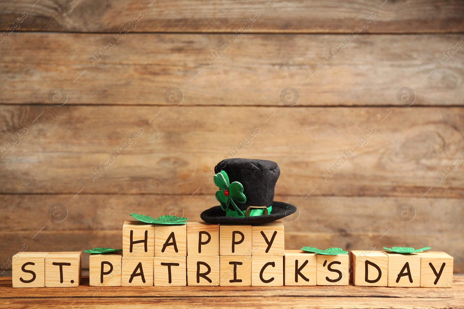 Photo of Leprechaun hat, clover leaves and wooden cubes with words Happy St Patrick's Day on table, space for text