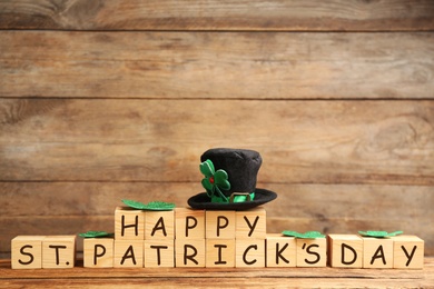 Leprechaun hat, clover leaves and wooden cubes with words Happy St Patrick's Day on table, space for text