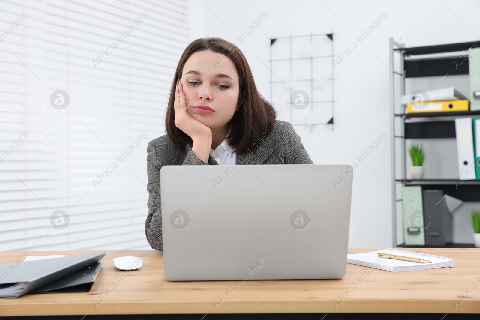 Photo of Puzzled young intern using laptop at table in modern office. First work day