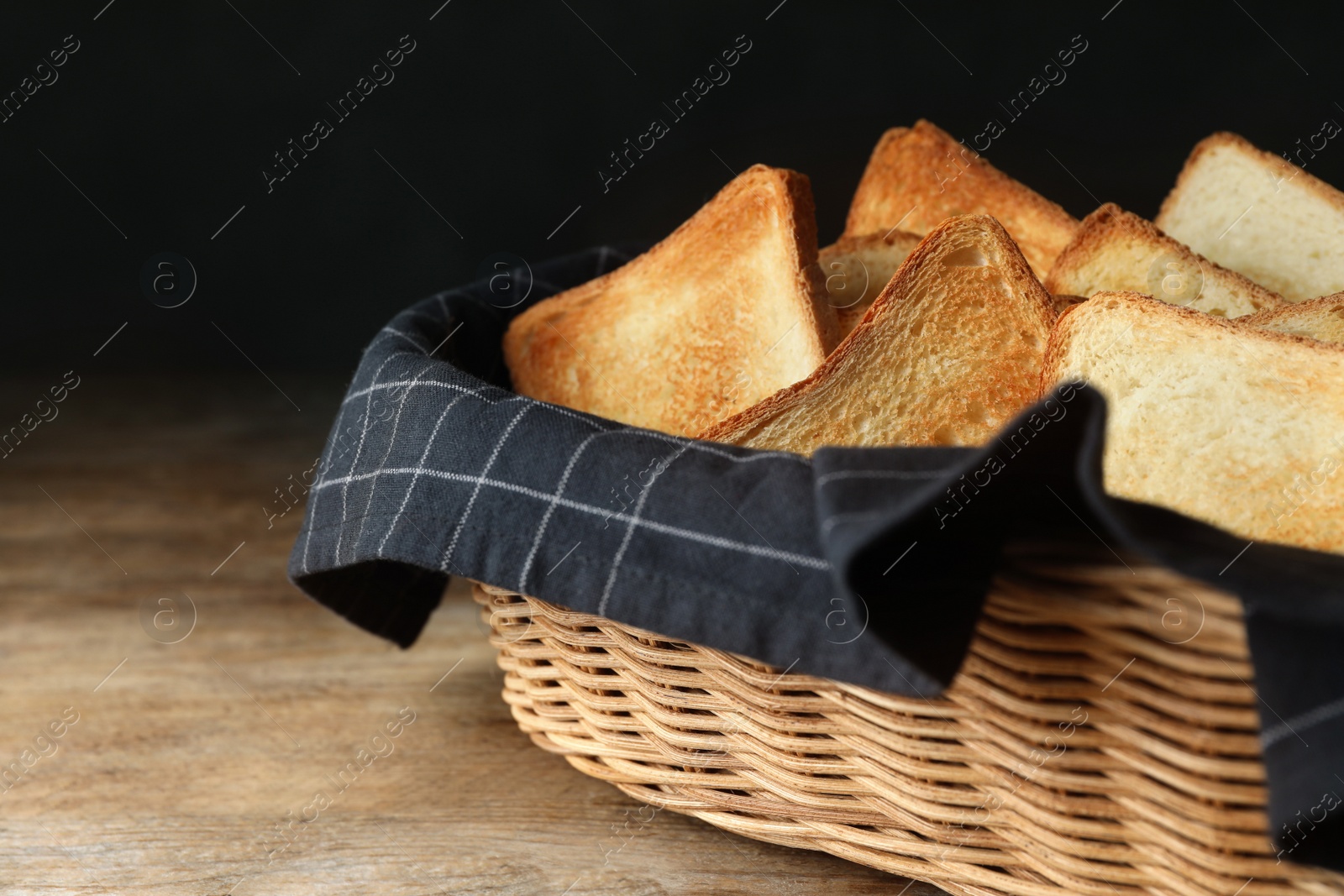 Photo of Slices of toasted bread in basket on wooden table against black background