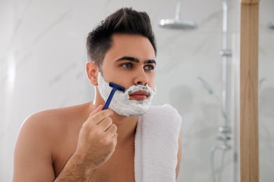 Photo of Handsome young man shaving with razor in bathroom