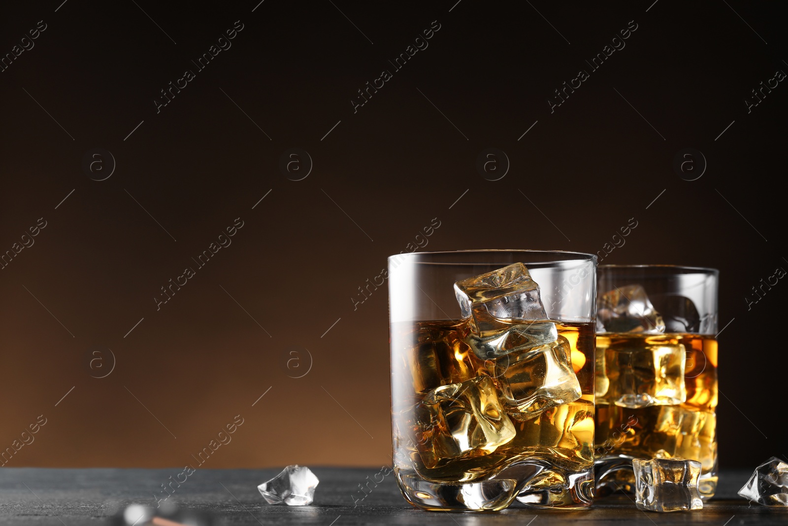Photo of Whiskey and ice cubes in glasses on black table, closeup. Space for text