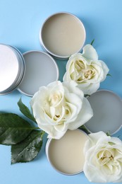 Different lip balms and rose flowers on light blue background, flat lay