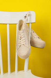 Pair of stylish sneakers hanging on white chair against yellow background