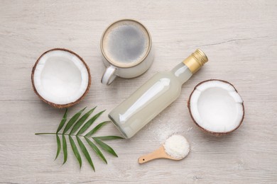 Photo of Bottle of delicious syrup, halves of coconut, flakes, cup of coffee and green leaves on white wooden table, flat lay