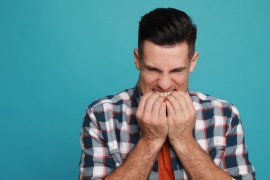 Man biting his nails on light blue background, space for text. Bad habit