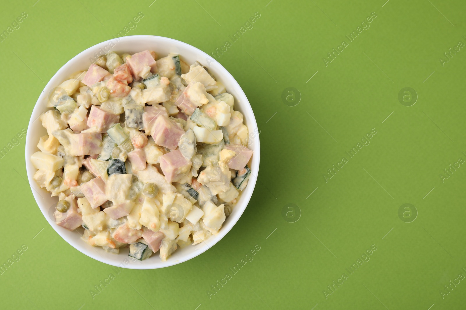 Photo of Tasty Olivier salad with boiled sausage in bowl on green table, top view. Space for text