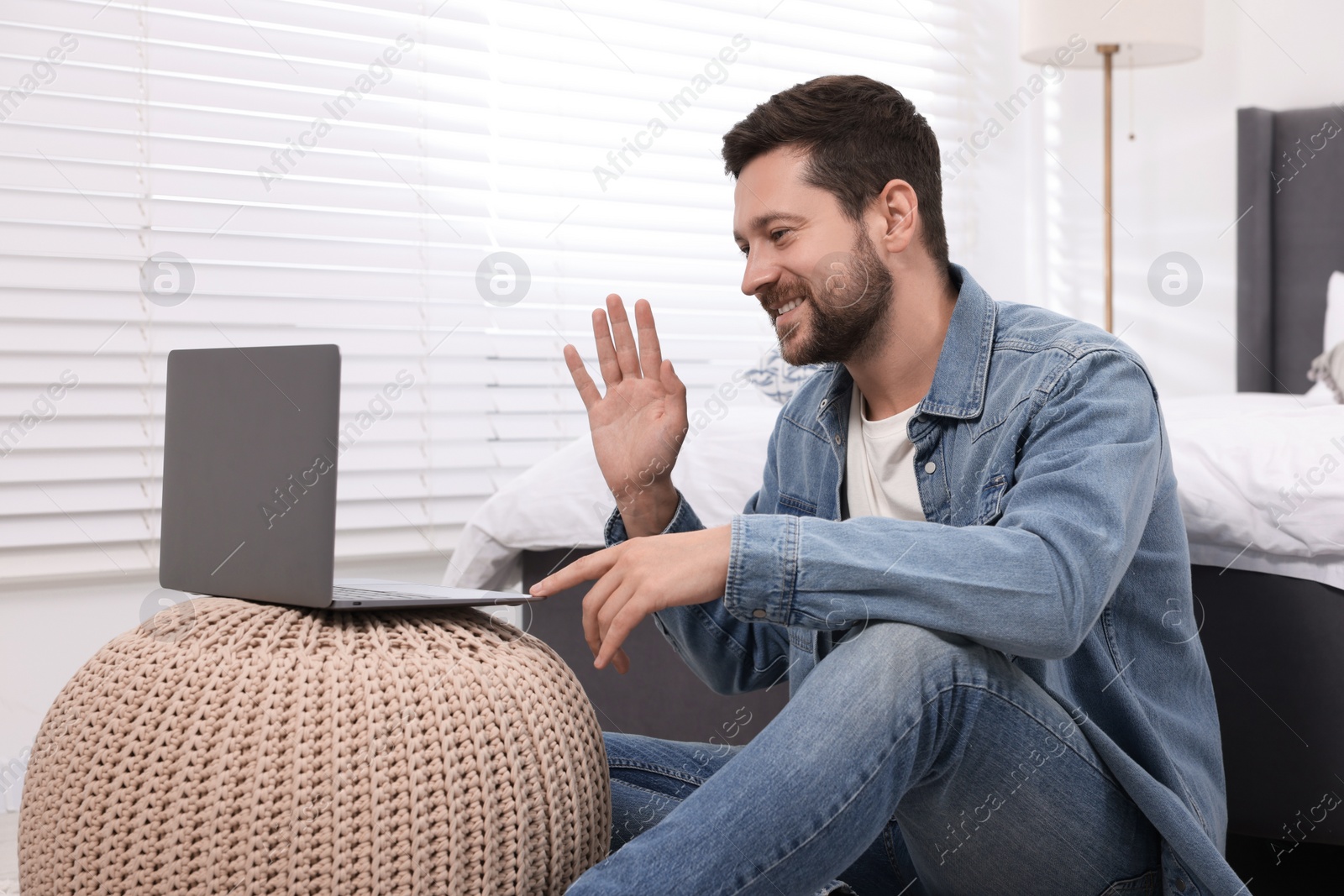 Photo of Happy man greeting someone during video chat via laptop at home