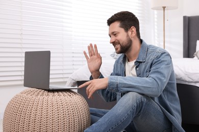 Photo of Happy man greeting someone during video chat via laptop at home