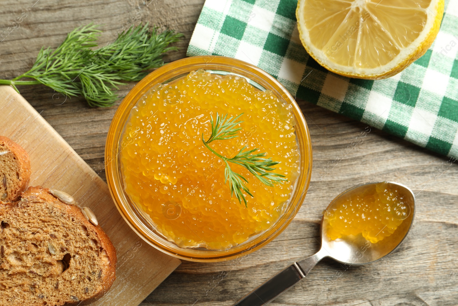 Photo of Fresh pike caviar in bowl, lemon and bread on wooden table, flat lay