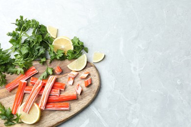 Delicious crab sticks with parsley and lemon on light grey marble table, flat lay. Space for text