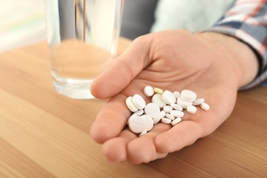 Man holding many pills in hand at table, closeup