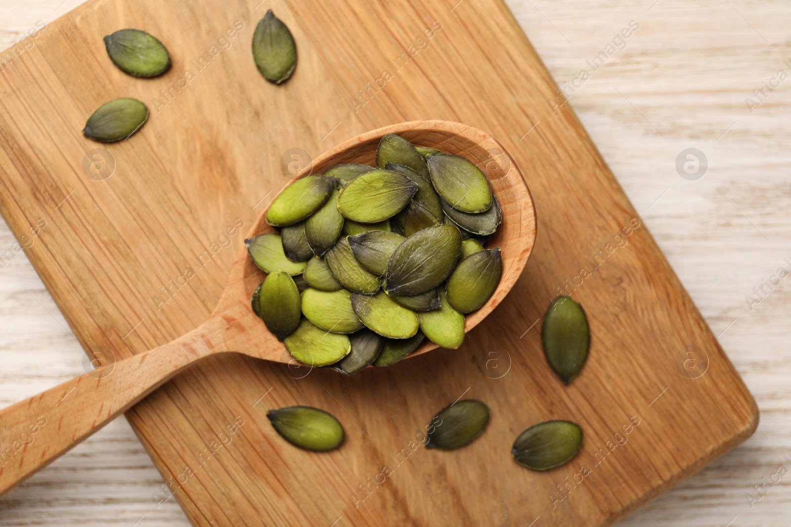 Photo of Spoon with pumpkin seeds on wooden table, top view