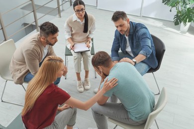 Psychotherapist working with group of drug addicted people at therapy session indoors