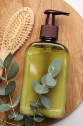 Shampoo bottle, hair brush and green leaves on white table, top view