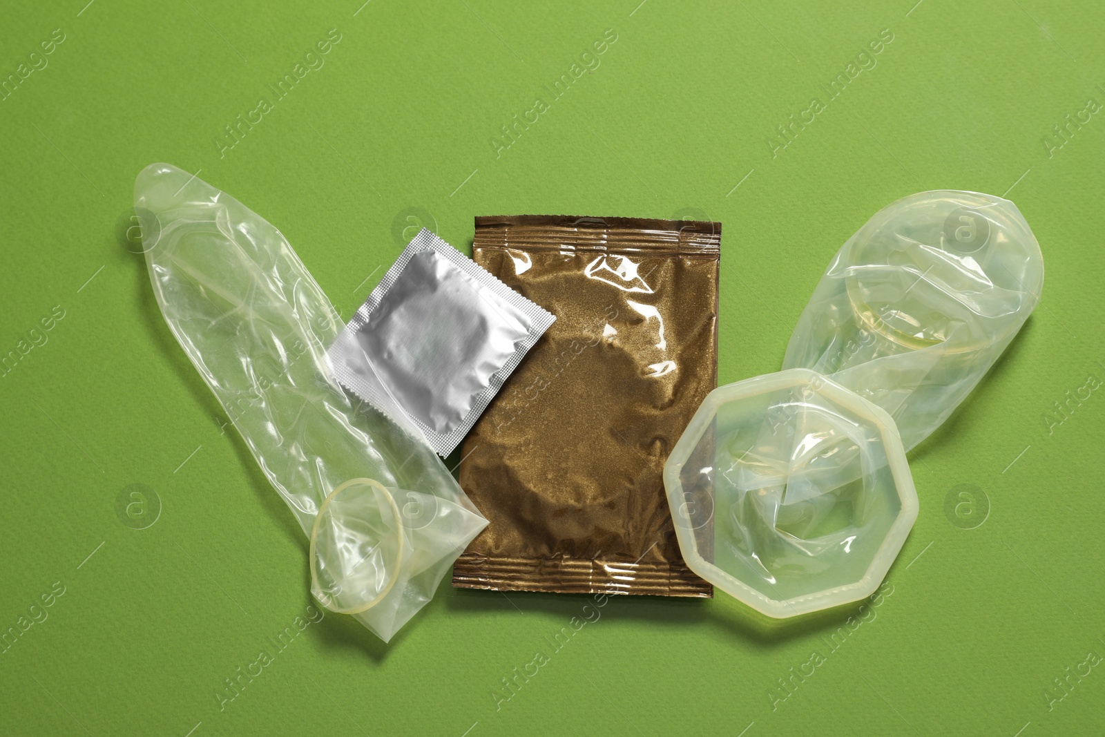 Photo of Unrolled female, male condoms and packages on green background, flat lay. Safe sex