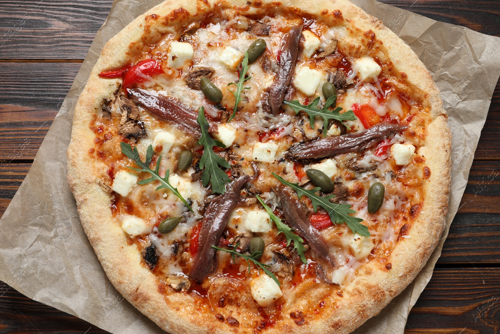 Photo of Tasty pizza with anchovies, arugula and olives on wooden table, top view