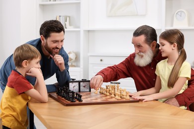 Photo of Family playing chess together at table in room