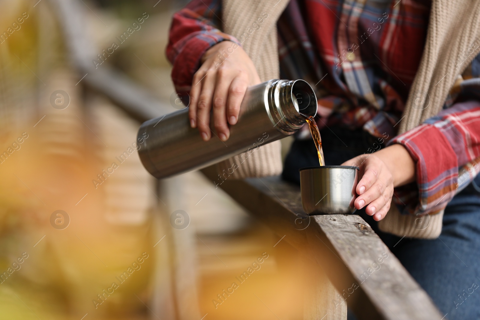 Photo of Woman pouring hot drink from metallic thermos into cup lid outdoors, closeup