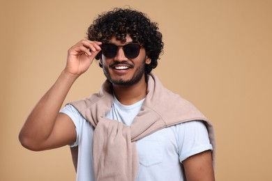 Handsome young smiling man in sunglasses on beige background