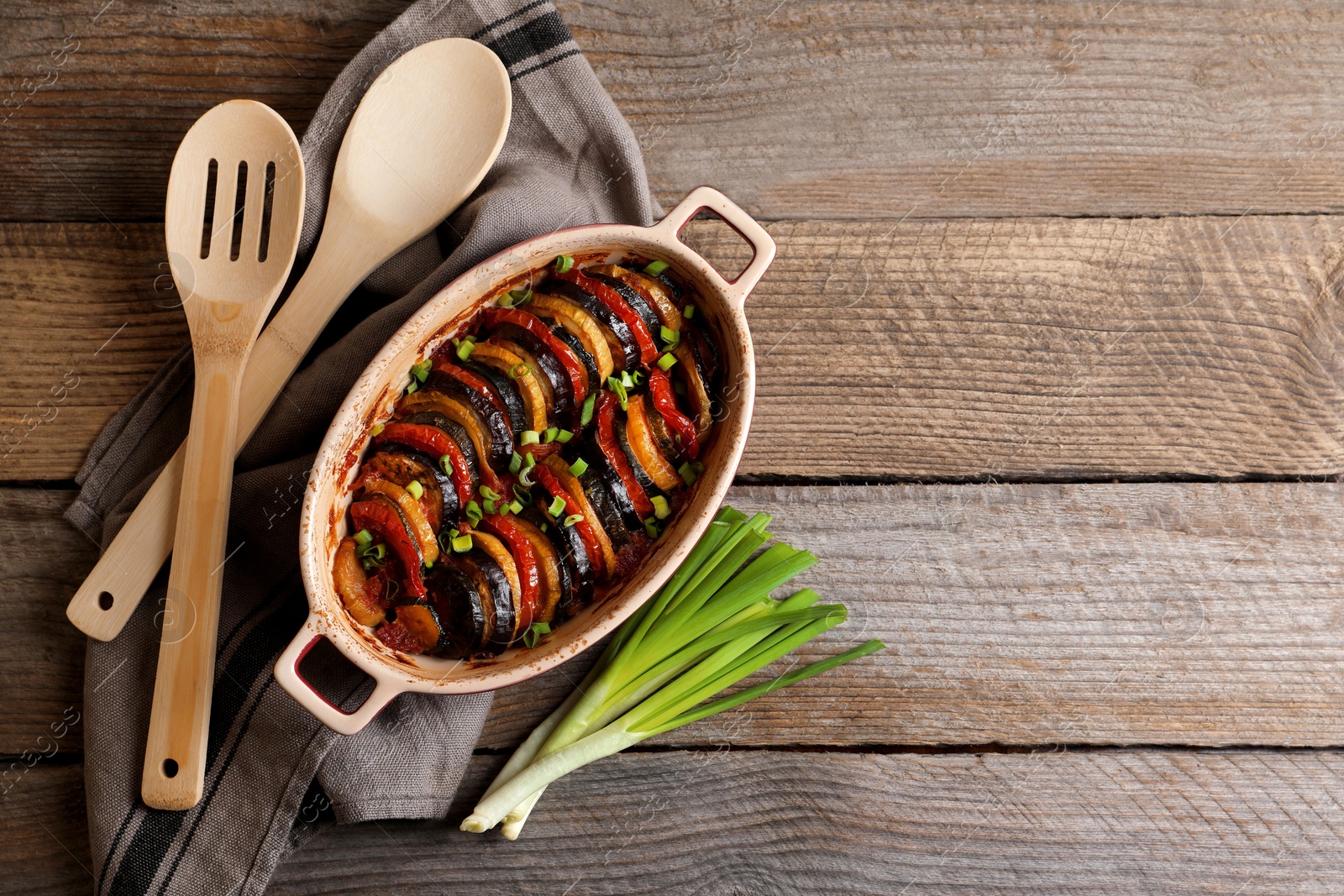 Photo of Delicious ratatouille, green onions, spoon and spatula on wooden table, flat lay. Space for text