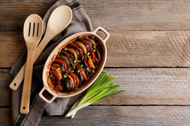 Delicious ratatouille, green onions, spoon and spatula on wooden table, flat lay. Space for text